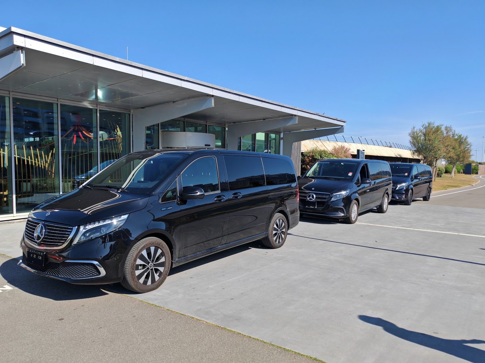 Trois Mercedes Classe V noires garées devant un bâtiment moderne
