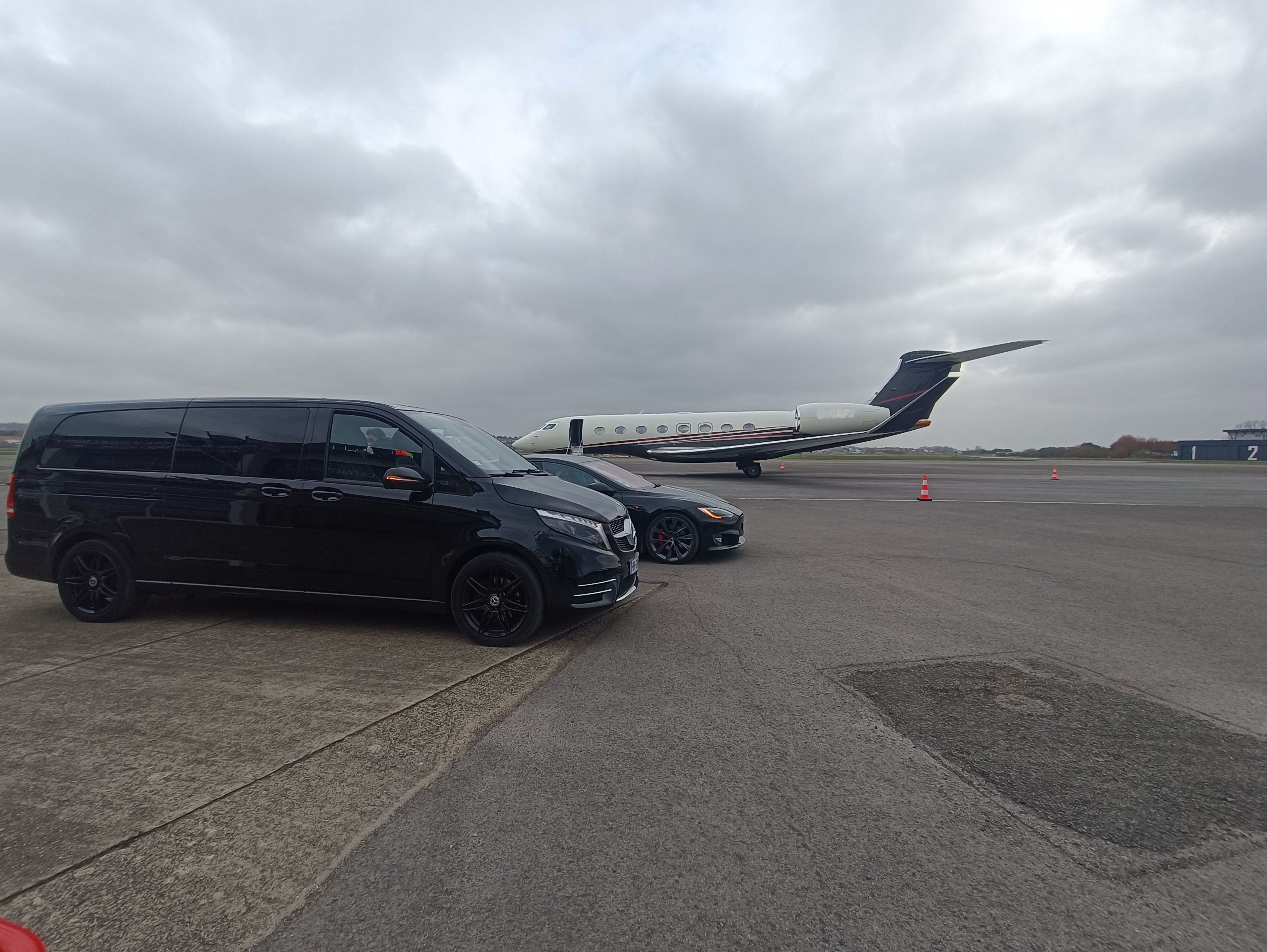 Mercedes Classe V et berline sur le tarmac devant un jet privé sombre